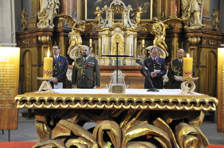 Asistující kaplani v čele vojenského kostela. Před nimi jsou desky s modlitbou za mír a modlitbou za padlé a zemřelé