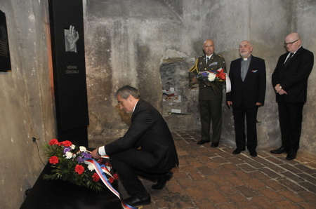 Ministr obrany položil kytici na pietní místo v kryptě chrámu a urovnává stuhy.