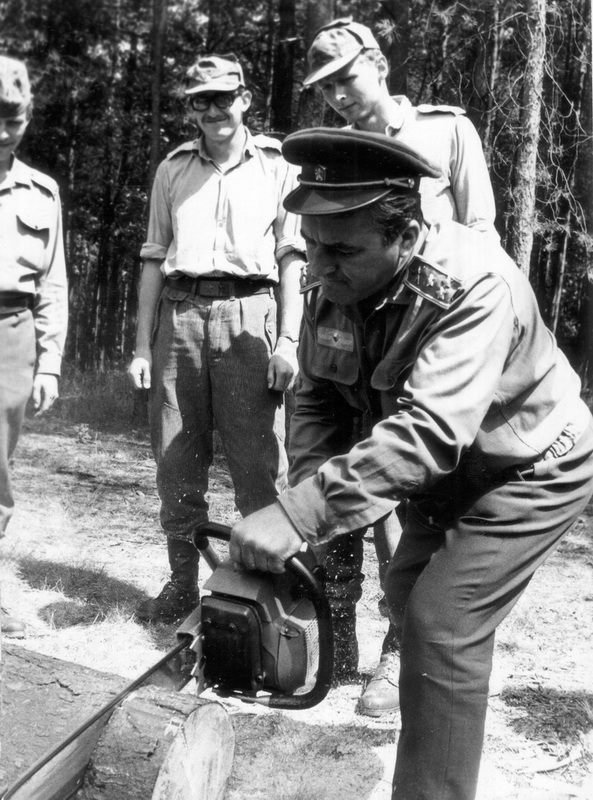 Náčelník vojenské katedry ČVUT ukazuje studentům práci s motorovou řetězovou pilou. Za pozornost stojí, že plukovník na snímku zcela ignoruje zásady bezpečnosti práce a neužívá žádné ochranné pomůcky. 70. léta.